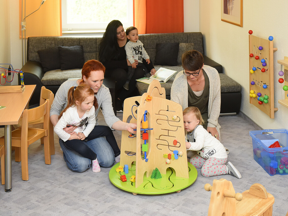 Drei Mütter und Ihre Kinder spielen gemeinsam in einem Aufenthaltsraum des Marianne van den Bosch Hauses.