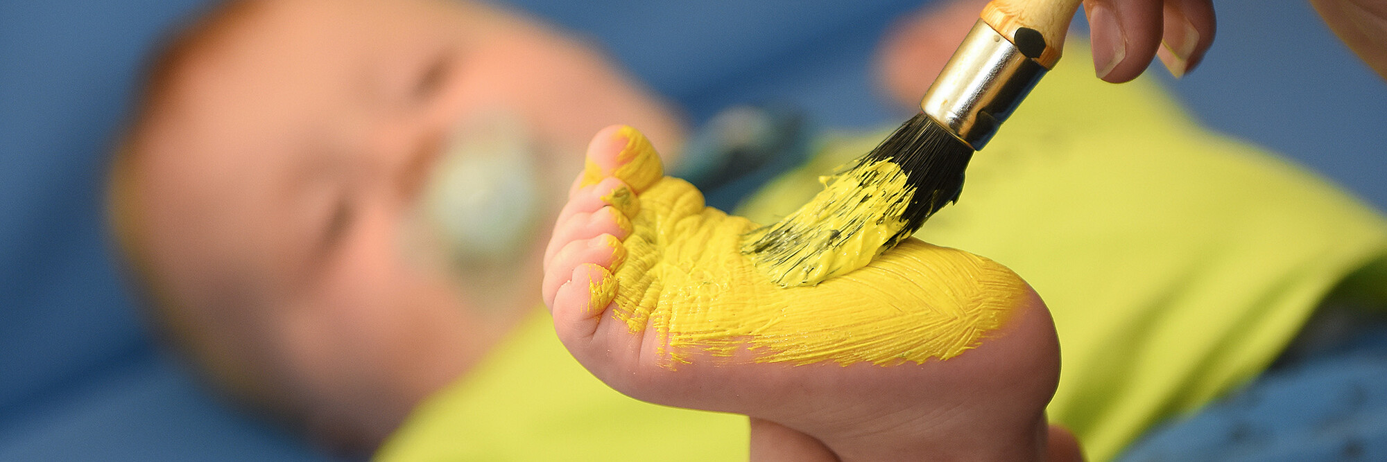 Der Fuß eines Kleinkindes wird im Rahmen einer Therapie mit gelber Farbe bepinselt.