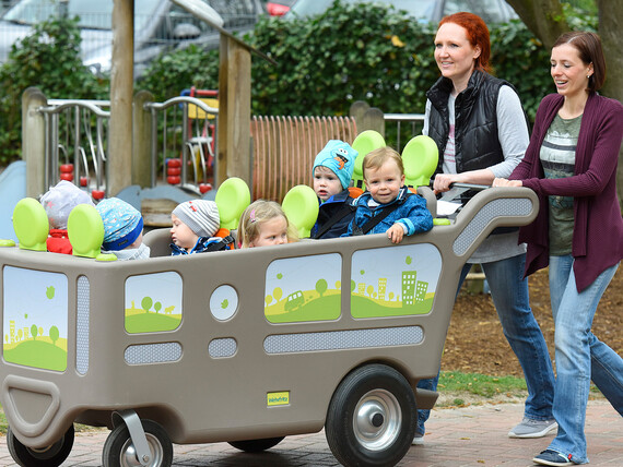 Zwei Mütter schieben fünf Kinder in einem großen Kinderwagen.