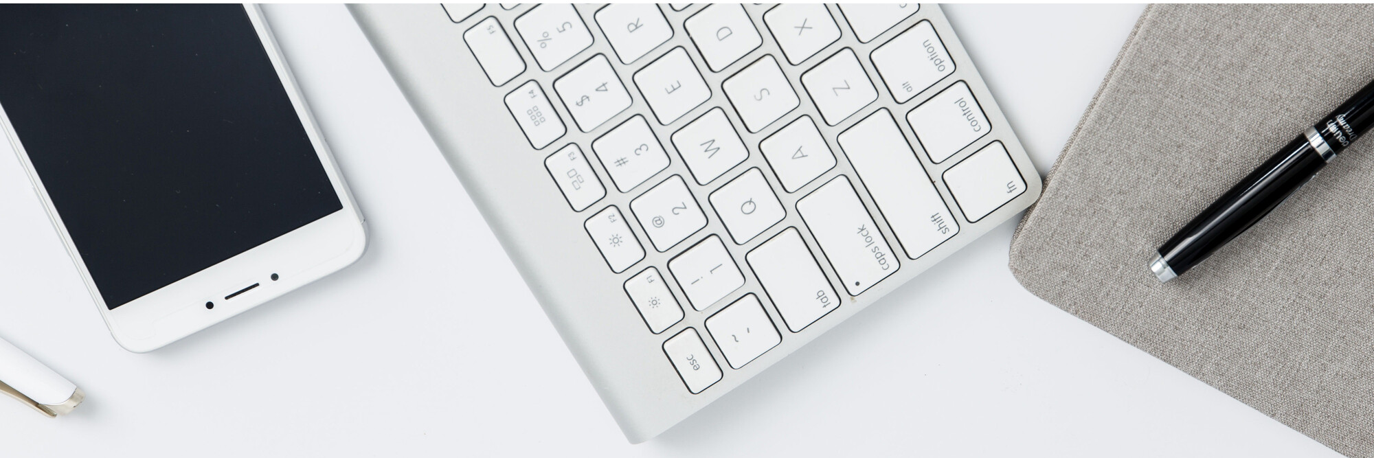 Blick auf einen Schreibtisch: Tastatur, Handy und Stift.