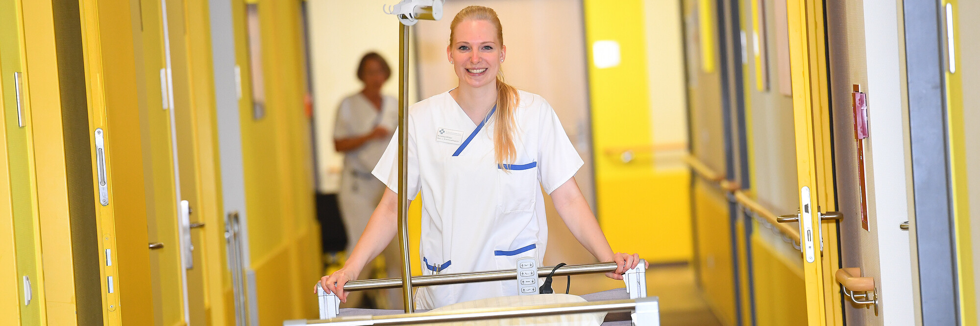 Eine Pflegerin des Katholischen Karl-Leisner-Klinikums schiebt lächelnd ein leeres Patientenbett über den Krankenhausflur.
