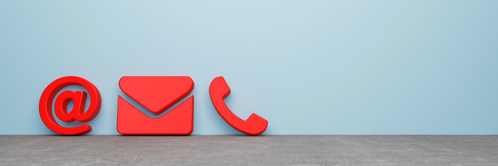 @-Zeichen, Mail-Zeichen und Telefonhörer lehnen als rote Symbole vor einer grauen Wand.