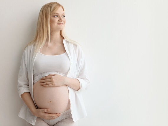 Eine glückliche Schwangere streichelt ihren Bauch und lächelt.