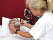 Eine Mitarbeiterin des Schlaflabors passt bei einem Patienten eine Sauerstoffmaske an.