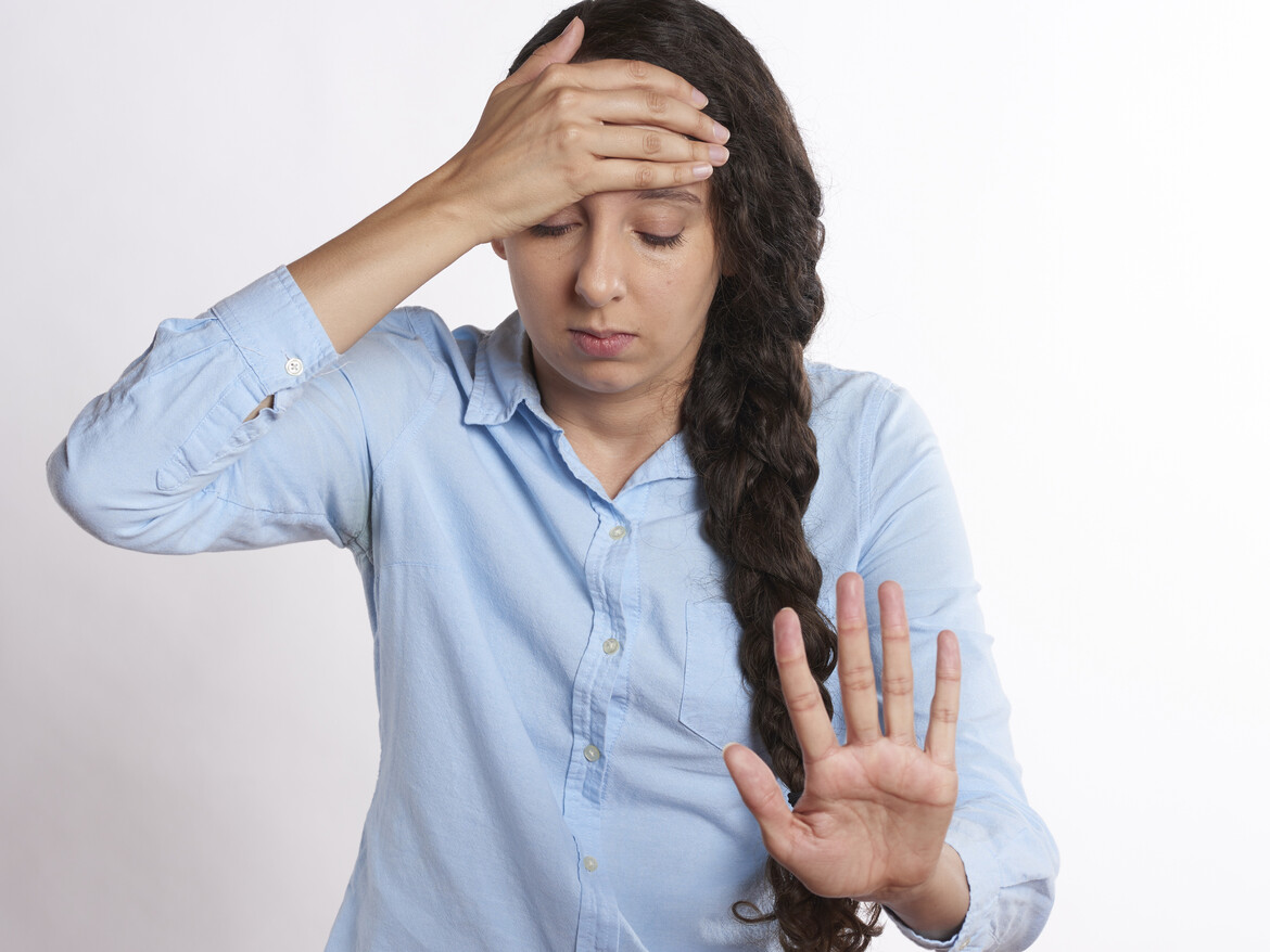 Eine junge Frau hält sich mit geschlossenen Augen den Kopf.