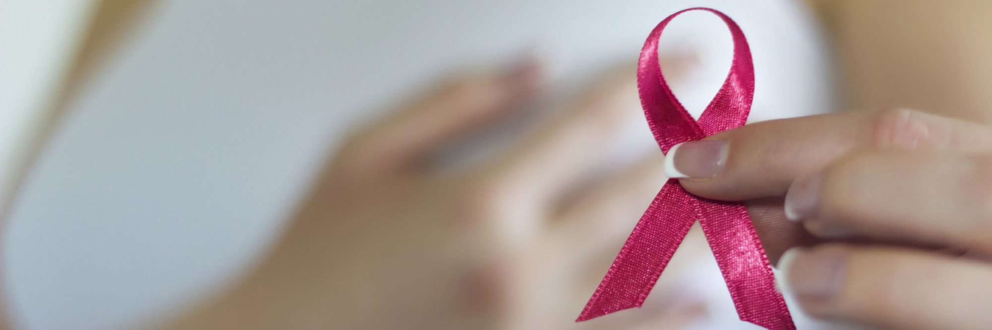 Frau hält eine rosa Schleife - ein internationales Symbol, mit dem auf die Problematik der Brustkrebserkrankung hingewiesen wird.