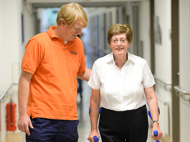 Ein Physiotherapeut unterstützt eine Patientin bei Gehübungen.