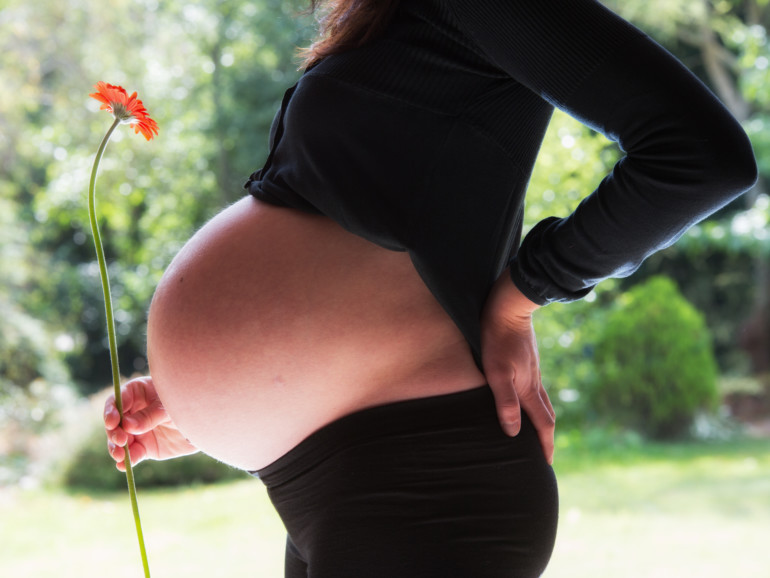 Eine Schwangere zeigt ihren Babybauch im Profil.