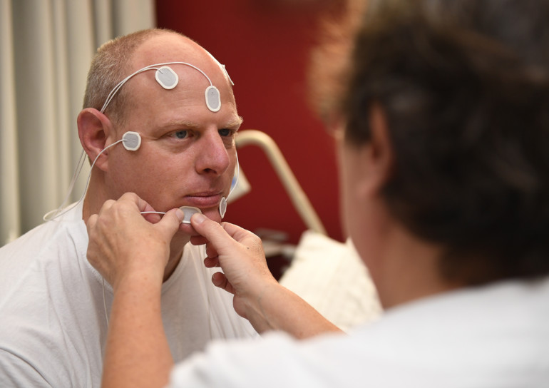 Eine Mitarbeiterin des Schlaflabors verkabelt einen Patienten für ein EKG.